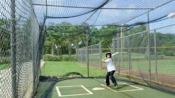 Disparo diurno en cámara lenta de un niño dentro de jaulas de bateo balanceándose en la pelota
 - Metraje, vídeo