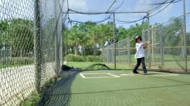 Disparo en cámara lenta de un niño pequeño bateando dentro de jaulas de bateo en el parque de béisbol durante el día
 - Metraje, vídeo