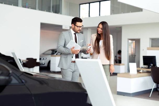 Professional salesperson selling cars at dealership to buyer - Фото, изображение