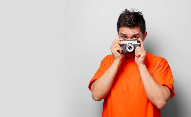 Nuori komea mies oranssissa t-paidassa, jossa on vintage-kamera. Studiokuva valkoisella taustalla
 - Valokuva, kuva