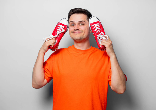 Młody przystojny mężczyzna w pomarańczowy t-shirt z czerwone Półbuty gumowe. Studio image na białym tle - Zdjęcie, obraz