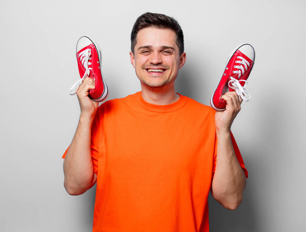 Joven hombre guapo en camiseta naranja con zapatos de goma rojos. Imagen del estudio sobre fondo blanco
 - Foto, Imagen