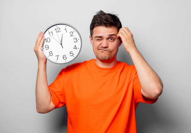 Young handsome man in orange t-shirt with big clock. Studio image on white background - 写真・画像