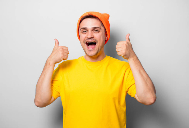 Fiatal jóképű férfi fehér alapon sárga pólót és narancssárga kalap - Fotó, kép