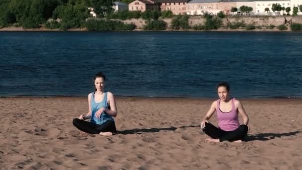 Deux femmes qui font du yoga sur la plage près de la rivière dans la ville et qui parlent. Belle vue
. - Séquence, vidéo