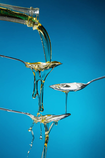 Pouring oil splash on spoons on blue background. Studio shooting - Zdjęcie, obraz