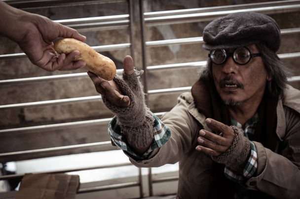 Close up of hand  giving bread to dirty homeless man on the street - Photo, Image
