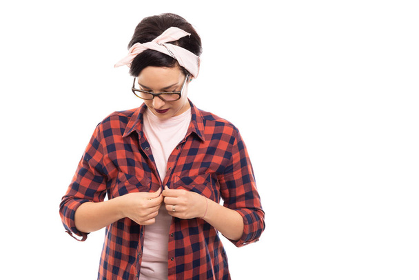 Porträt eines jungen hübschen Pin-up-Mädchens mit Brille, das Hemd auf weißem Hintergrund mit Copyspace-Werbefläche zuknöpft - Foto, Bild