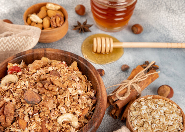 Homemade granola in wooden bowl with ingredients - oat, nuts, honey and spice cinnamon and anise. - Photo, image