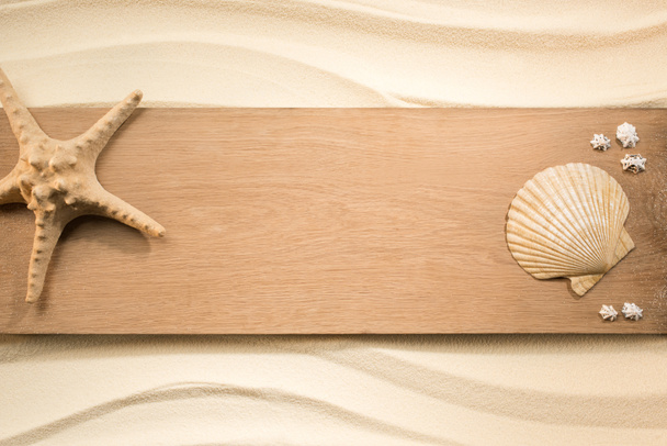flat lay with arrangement of sea star and seashells on wooden plank on sand - Photo, Image