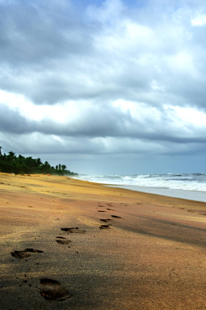 Footprints on a deserted beach in Sri Lanka. Above the stormy ocean, a gloomy cloudy sky with heavy clouds. - 写真・画像