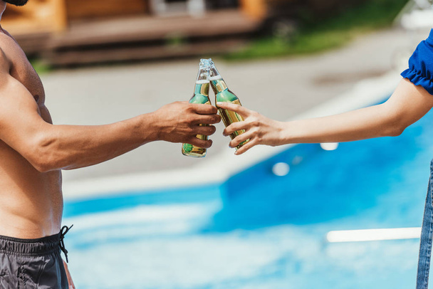 cropped view of couple clinking with bottles of beer at poolside - Foto, Imagem