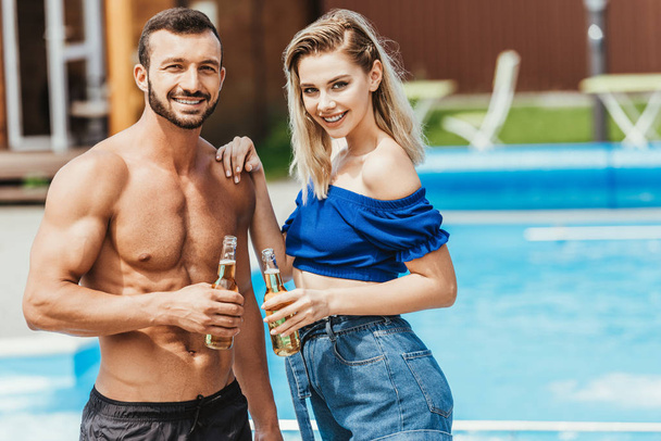 ευτυχισμένο ζευγάρι όμορφα με μπουκάλια μπύρας δίπλα στην πισίνα  - Φωτογραφία, εικόνα