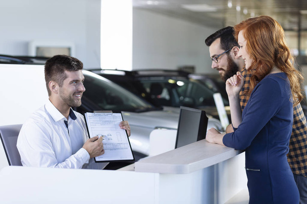 Smiling car dealer showing rental agreement to buyers in the showroom - Zdjęcie, obraz