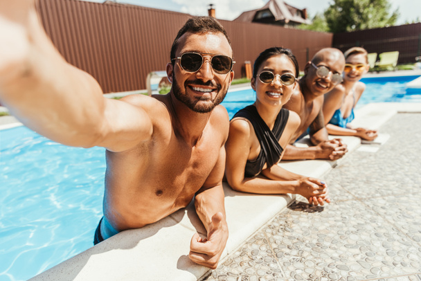 souriant amis multiculturels dans des lunettes de soleil prendre selfie dans la piscine
 - Photo, image