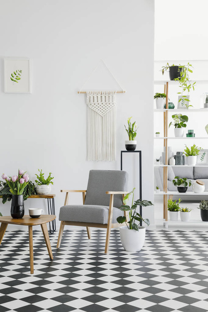 Checkered floor in a retro living room interior with white walls, plants, armchair and coffee table. Real photo - Fotoğraf, Görsel