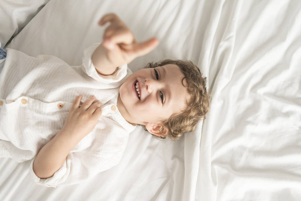 Child lying on the bed playing and gesturing. - 写真・画像