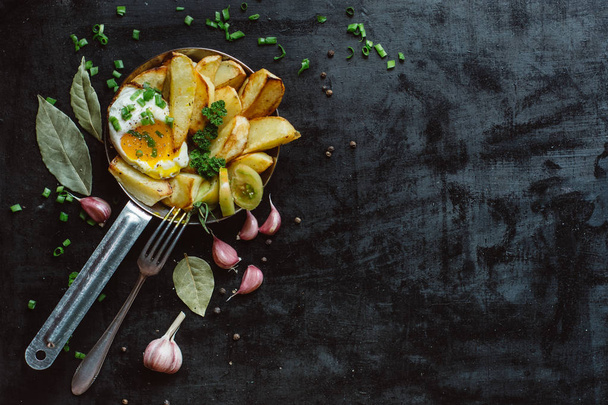  Breakfast in pan with fried eggs, potatoes, fresh herbs  on dark  background copy space - Zdjęcie, obraz