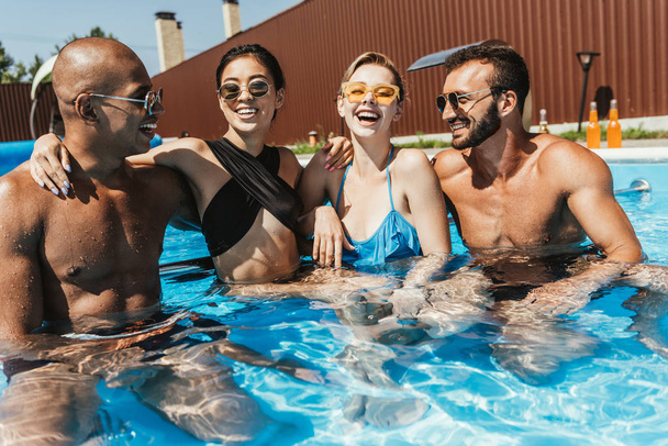 Смеющиеся мультиэтнические пары в солнцезащитных очках проводят время в бассейне
 - Фото, изображение