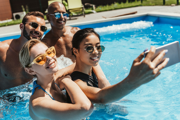 スイミング プールでのスマート フォン selfie を取ってサングラスでは多文化のカップル - 写真・画像
