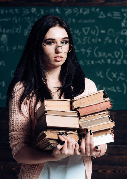 Lovely female student with heap of books standing in classroom. Brunette college girl cramming before exams - Foto, Imagen