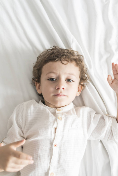 Child lying on the bed playing and gesturing. - 写真・画像