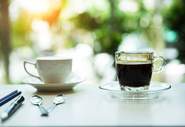 Primer plano de la taza de café negro puesto en la mesa en la cafetería, luz borrosa alrededor
. - Foto, Imagen