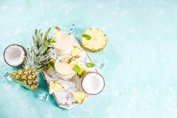 Refreshing summer drink, homemade pina colada cocktail, on a light blue background, with pieces of pineapple, coconut, ice and mint leaves, copy space top view - Фото, изображение