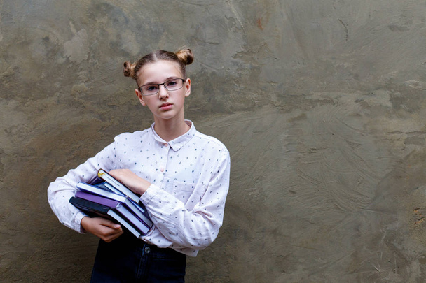 Középiskolában, Egyetemen súlyos fiatal lány gazdaság könyvek. Betonfal szürke háttér. Oktatási koncepció - Fotó, kép