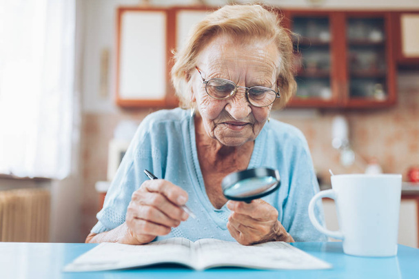 Senior woman in her 80s enjoys solving a crossword puzzle - Фото, изображение