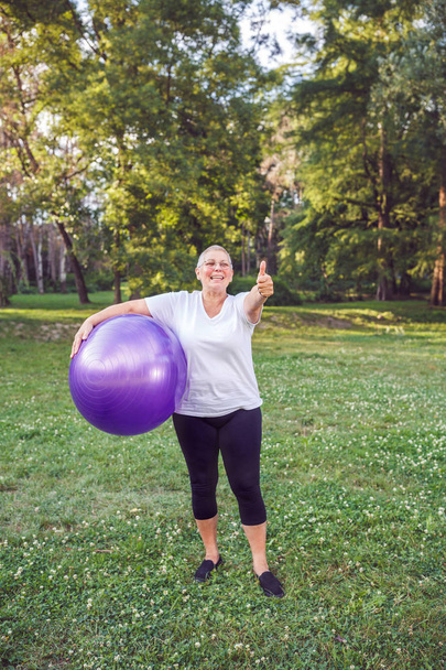 palec pro zdravé cvičení - šťastný důchodce žena s fitness míče v parku a cvičení - Fotografie, Obrázek
