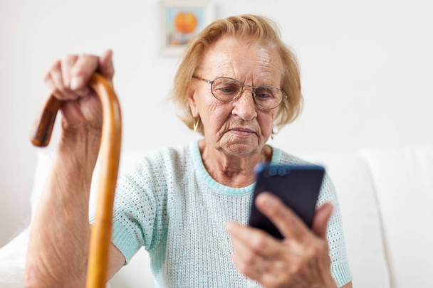 Elderly woman with glasses and cane using a mobile phone - Fotografie, Obrázek