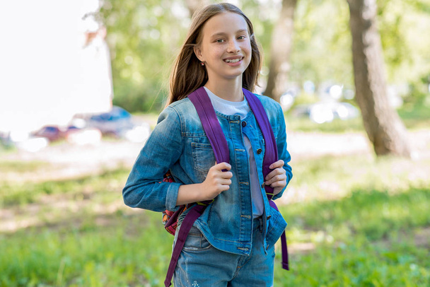 A schoolgirl girl is smiling in summer in park. Behind the backpack. Concept back to school. Emotions of happiness and smiles. - Valokuva, kuva