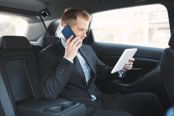 Executive businessman sitting at the back of car using a mobile phone - Zdjęcie, obraz