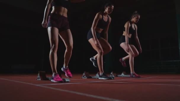Vrouwelijke lopers op atletiek bijhouden gehurkt op de startblokken voor een race. In slow motion. - Video
