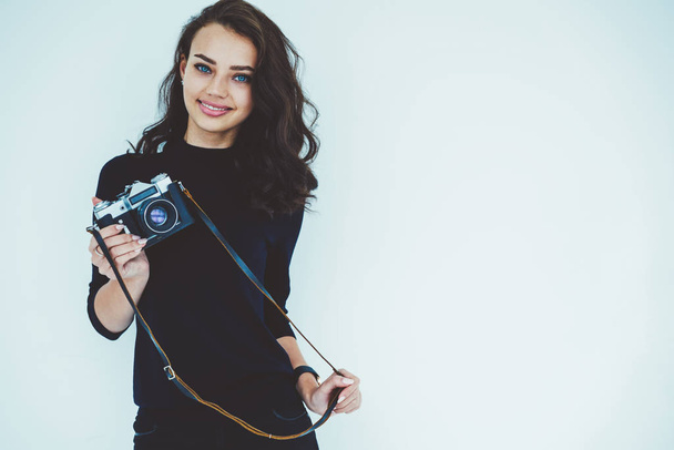Half length portrait of attractive female  professional with blue eyes holding vintage camera in hand and smiling at camera standing on white promotional background for your advertising text message - Zdjęcie, obraz