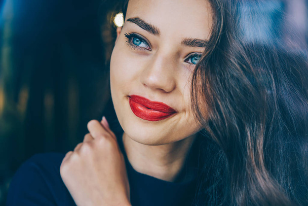Cropped close up image of charming young woman 20 years old dreaming and thinking on creative ideas.Attractive brunette female with red lips and beautiful blue eyes looking away with smile on face - Zdjęcie, obraz