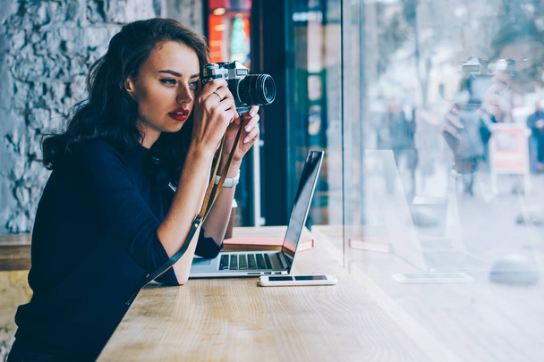 Ammattimainen nuori valokuvaaja tekee valokuvia vintage-kameralla julkaistavaksi omalla verkkosivustolla istuu kahvilassa puupöydässä kannettavalla tietokoneella, joka yhdistää langattomaan suureen nopeuteen 4G internet
 - Valokuva, kuva