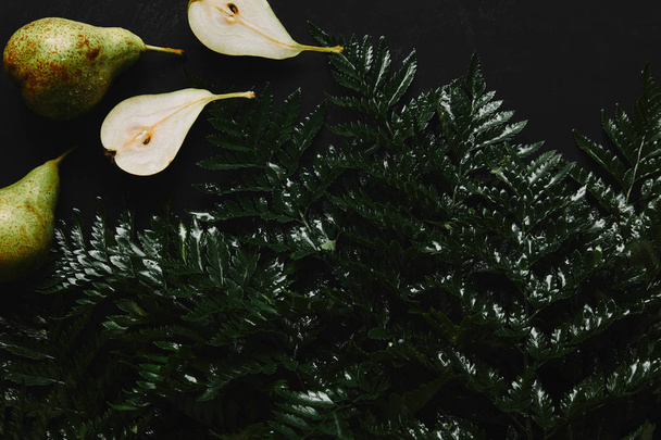 bovenaanzicht van hele en gesneden peren en natte fern op zwart - Foto, afbeelding