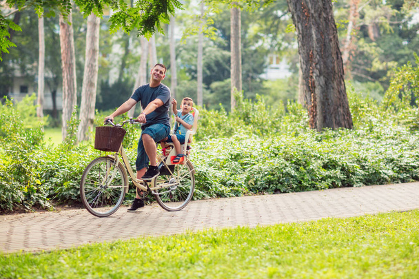 Happy family. Happy father and son riding a bicycle together outdoors in a city park - Photo, Image