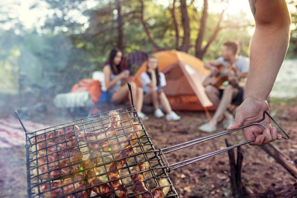 Party, camping of men and women group at forest. They relaxing, singing a song and cooking barbecue - Фото, изображение