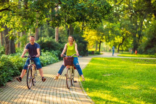 Onnellinen perhe. Hymyilevä aktiivinen isä ja äiti, jolla on lapsi polkupyörillä hauskaa puistossa
. - Valokuva, kuva