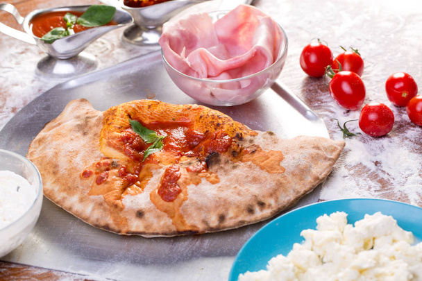 Close up of tasty calzone pizza with ingredients on a wooden table - Photo, image
