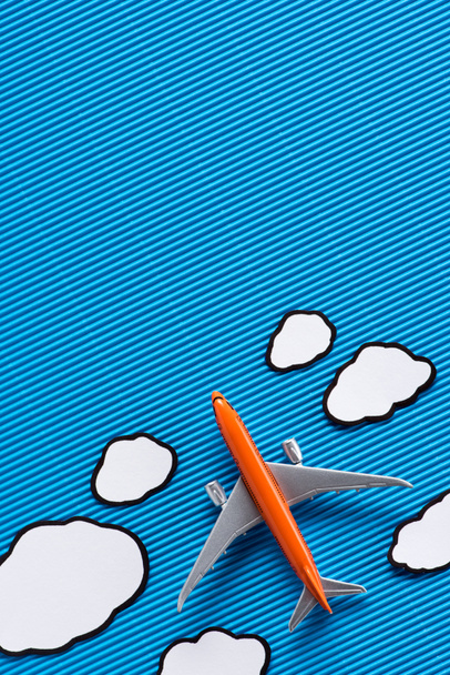 top view of toy plane and paper clouds on blue backdrop, trip concept - Foto, afbeelding