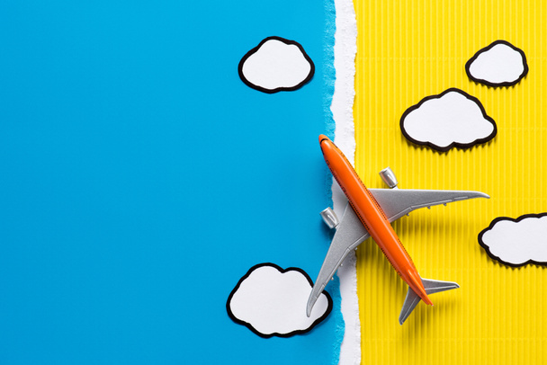 top view of toy plane and paper clouds on yellow and blue background, trip concept - Photo, Image