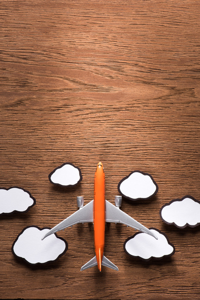 top view of toy plane and paper clouds on wooden surface, traveling concept - Photo, Image