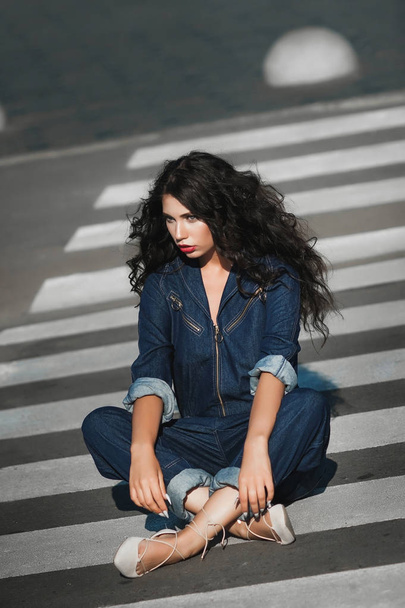 girl in jeans jumpsuit sits on a pedestrian crossing - 写真・画像