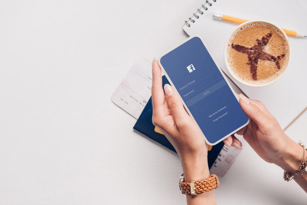 コーヒー、航空券とパスポートをスマート フォン画面で卓上で facebook のロゴを持つ女性のショットをトリミング - 写真・画像