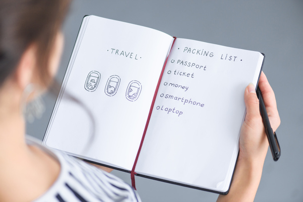 partial view of woman with pen holding notebook with packing list for traveling - Photo, image
