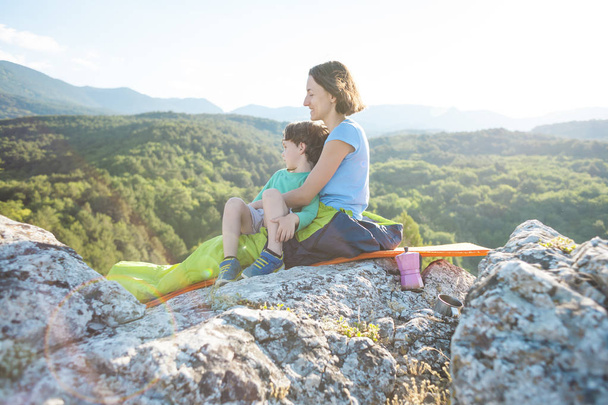 Camping on top of the mountain. Mom and child are traveling together. A woman and her son rest after climbing. The girl in the sleeping bag. Maternal embrace. - Photo, image